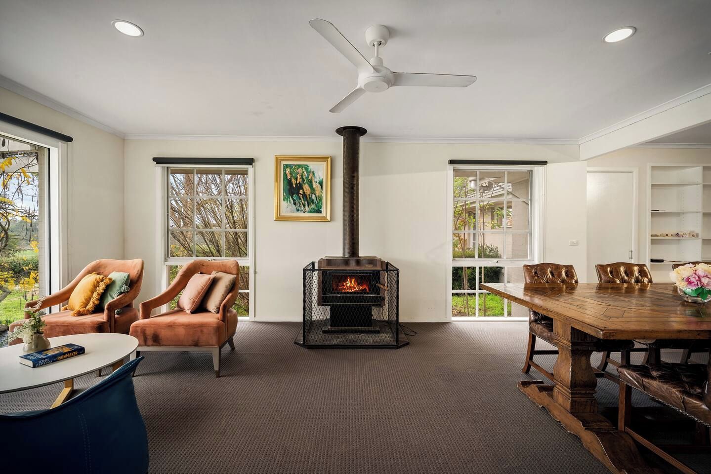 A modern living room with a fireplace, leather chairs, a dining table, and large windows.