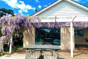 A covered outdoor area with a table and chairs, surrounded by purple wisteria vines. - Yarra Valley Farmhouse | Alpacas Firepit Space Pod (Wonga Park)
