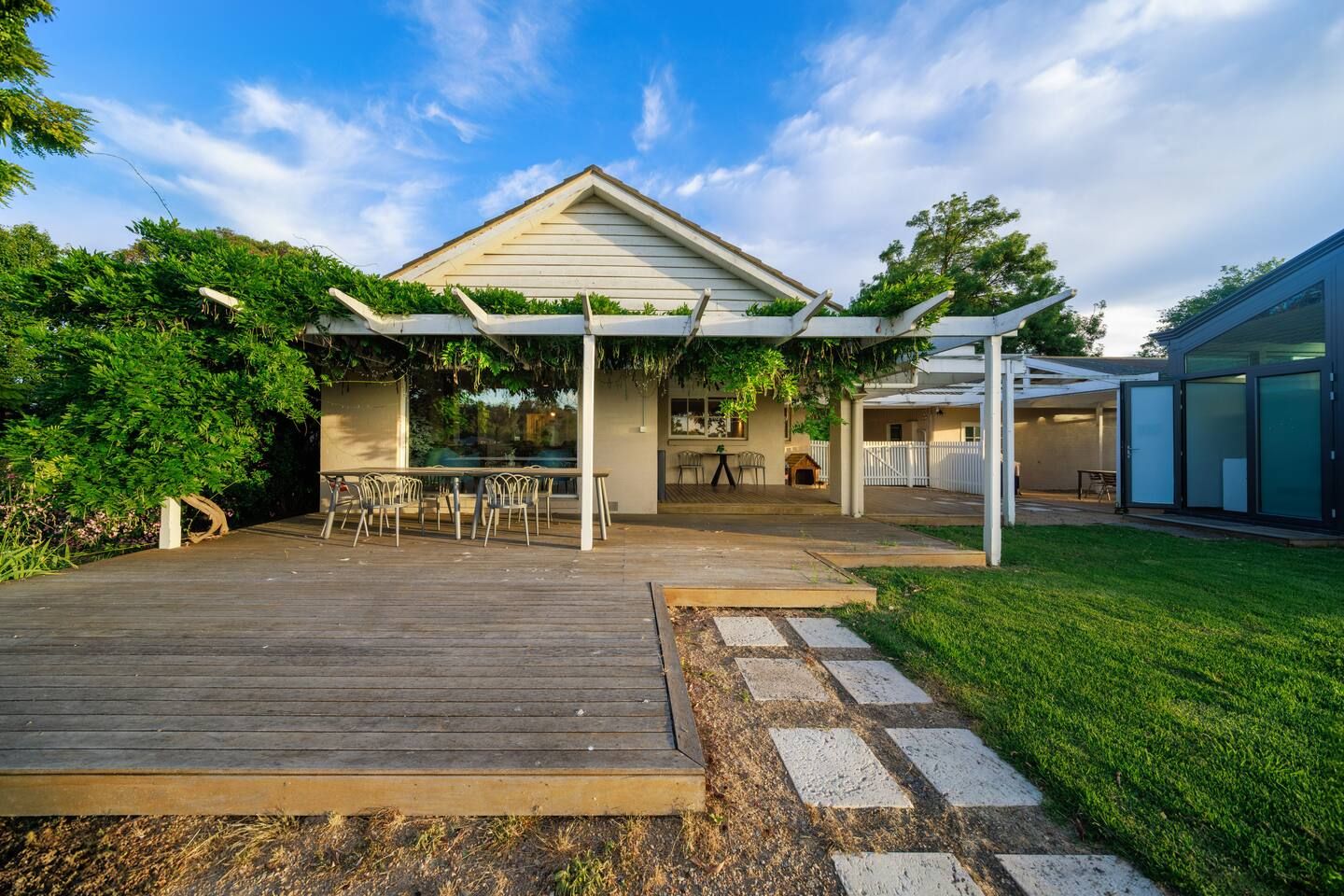 Una casa con terraza de madera, un patio cubierto y un patio trasero cercado.