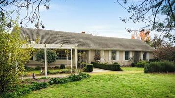 A two-story building with a covered patio area, surrounded by a well-maintained garden with various plants and shrubs.
