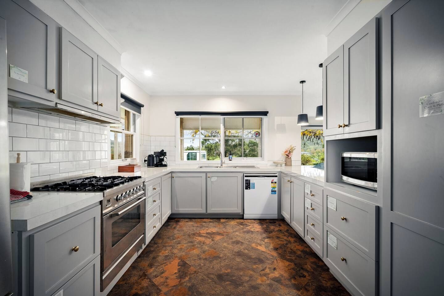A modern kitchen with grey cabinets, a stainless steel stove, and a large window.