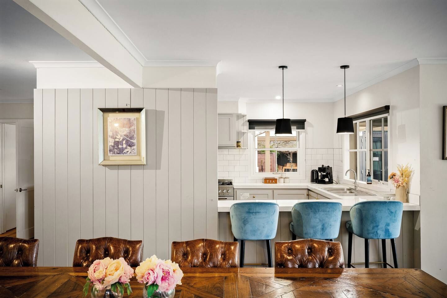 A modern kitchen with white cabinetry, a central island with bar stools, and a dining area with a wooden table and chairs.