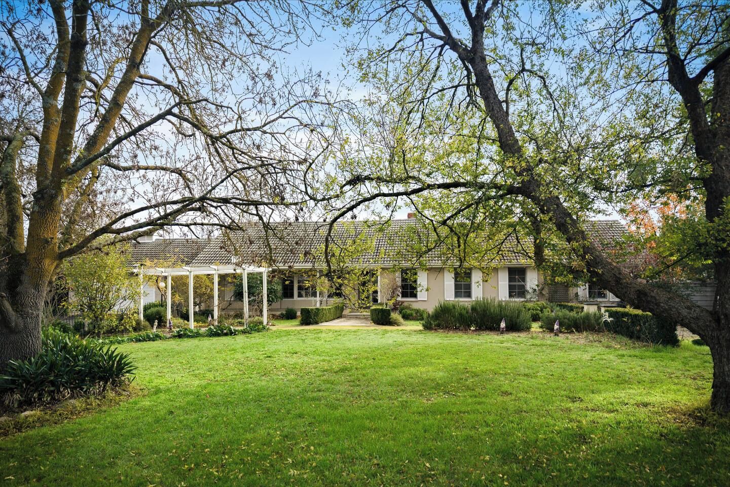 A house with a covered patio, surrounded by a well-maintained lawn and mature trees.