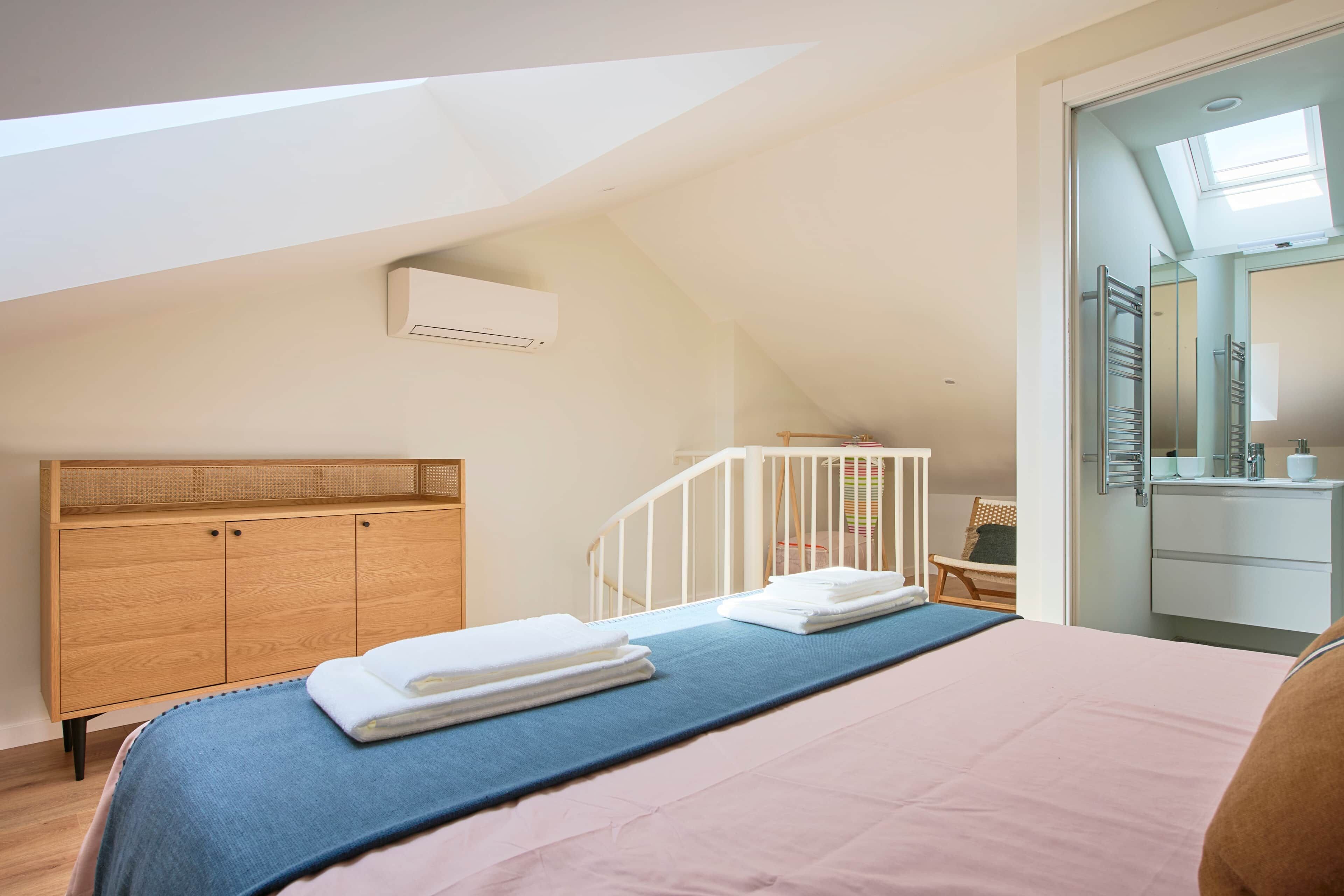 Un dormitorio con techo inclinado, una cuna, un tocador con espejo y una cama con toallas.