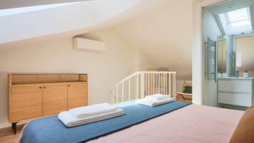 Un dormitorio con techo inclinado, una cuna, un tocador con espejo y una cama con toallas.