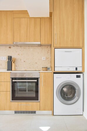 Een moderne keuken met houten kastjes, een inbouwoven, een wasmachine en een magnetron.