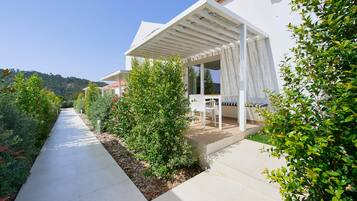Een modern huis met een overdekt terras, een pad en weelderige begroeiing.