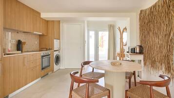 Cocina moderna con armarios de madera, horno empotrado y lavadora. Hay una mesa de comedor redonda con cuatro sillas de mimbre.