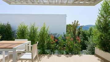 Un patio exterior con una mesa y sillas, una pérgola arriba y vistas a zonas verdes y colinas.