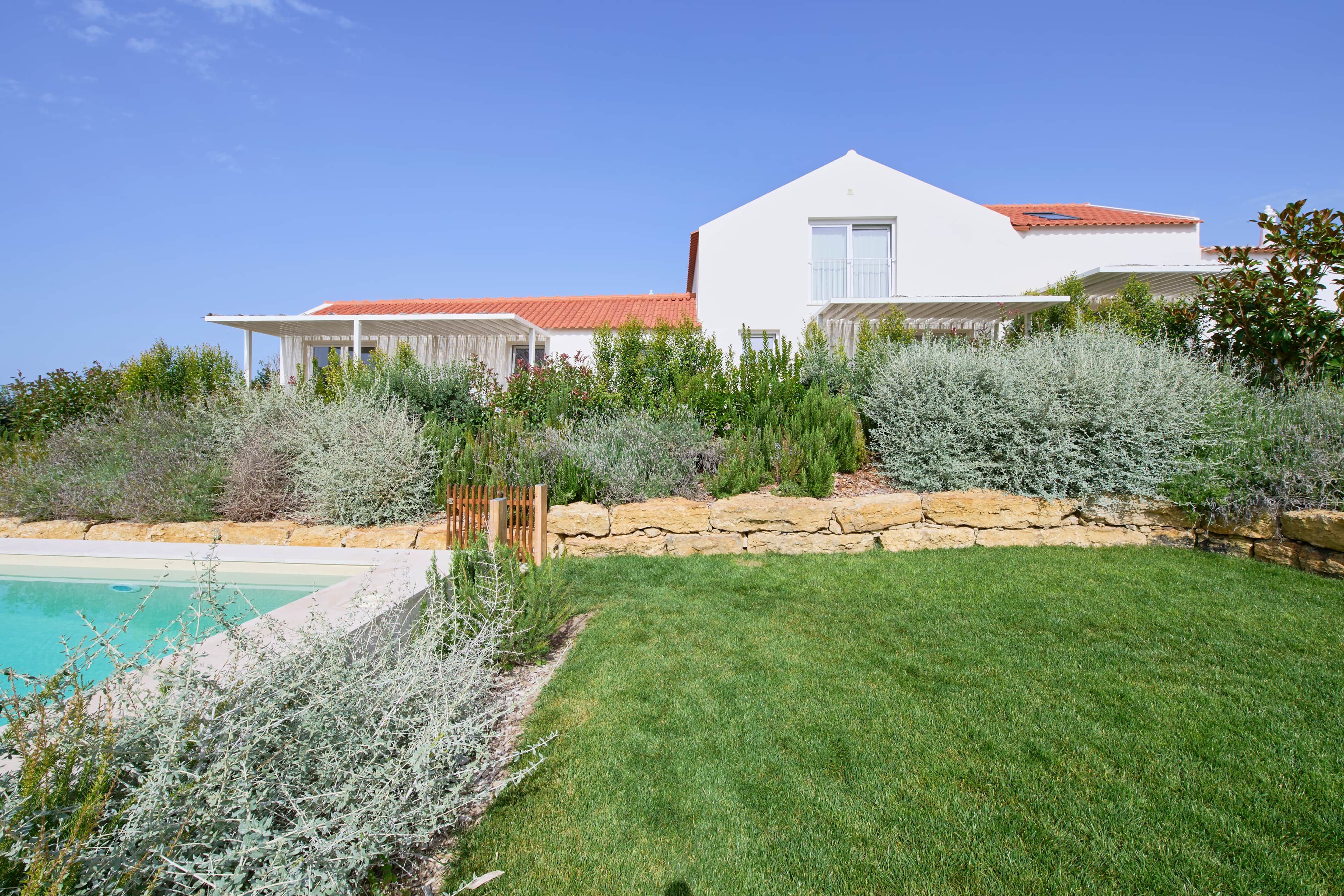 Una casa moderna con piscina, rodeada de césped y arbustos cuidados.