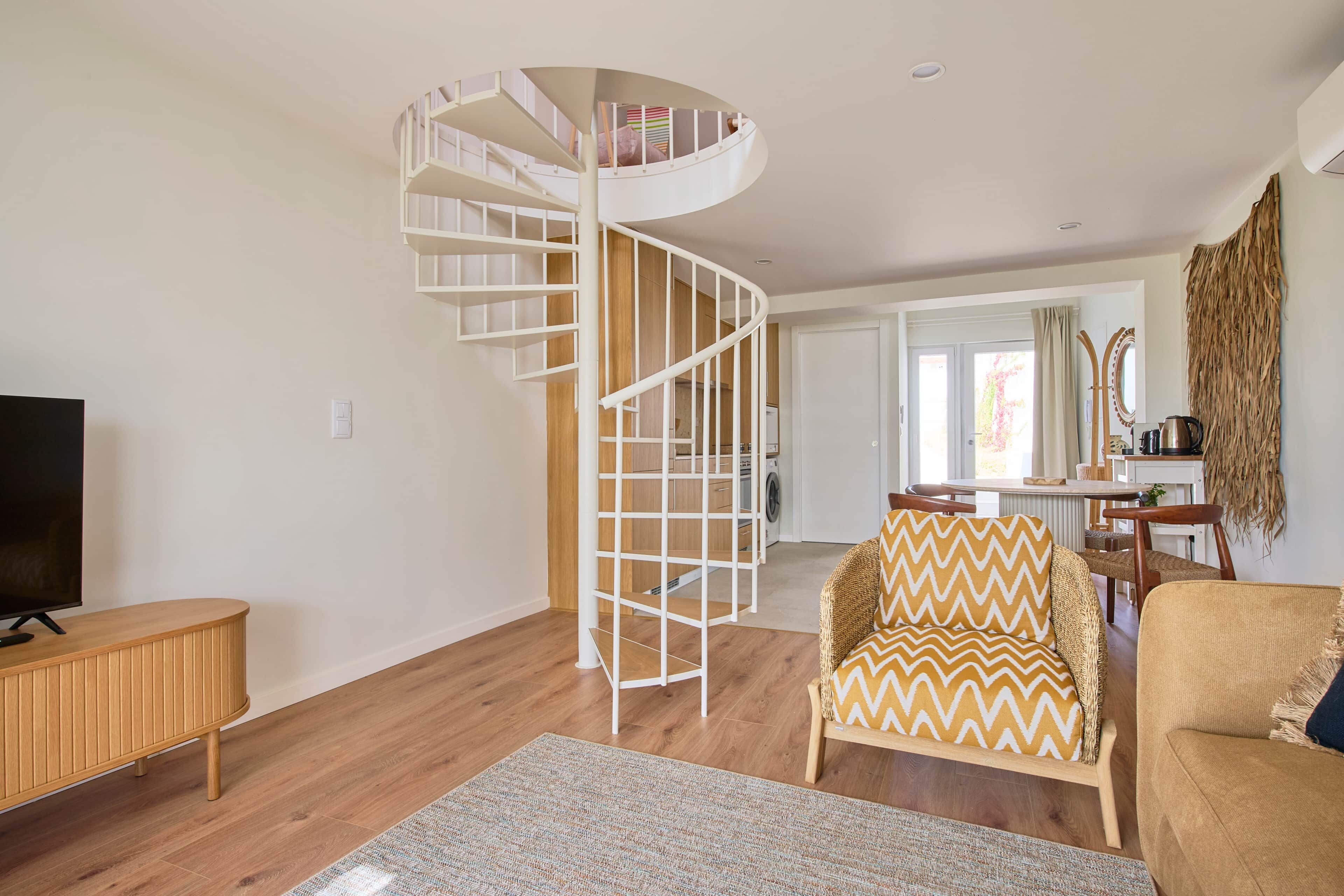 Una sala de estar moderna con una escalera espiral, piso de madera, un mueble para televisión y un comedor.