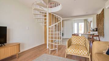 Una sala de estar moderna con una escalera espiral, piso de madera, un mueble para televisión y un comedor.