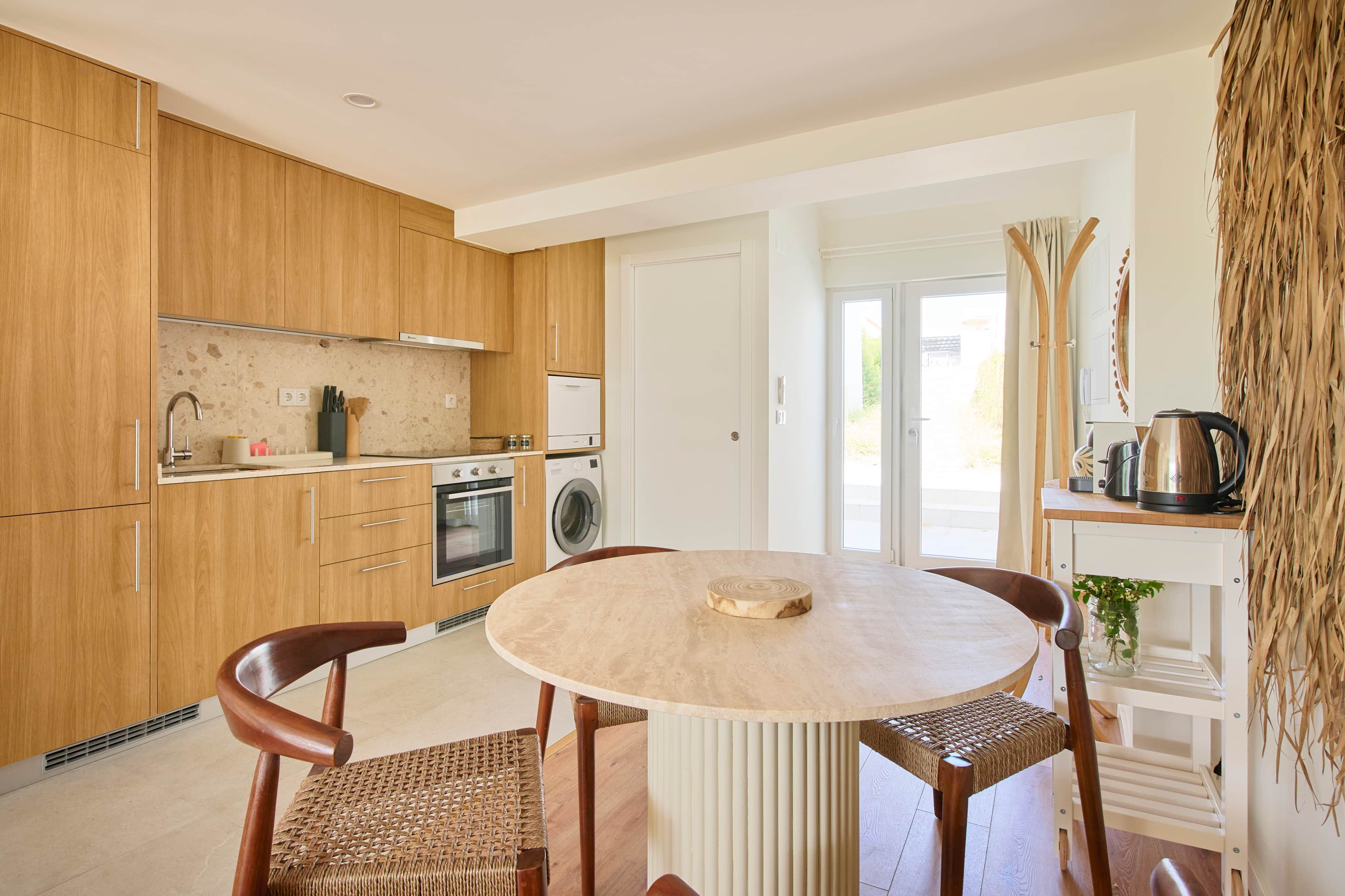 Una cocina moderna con armarios de madera, una mesa redonda y un horno empotrado.