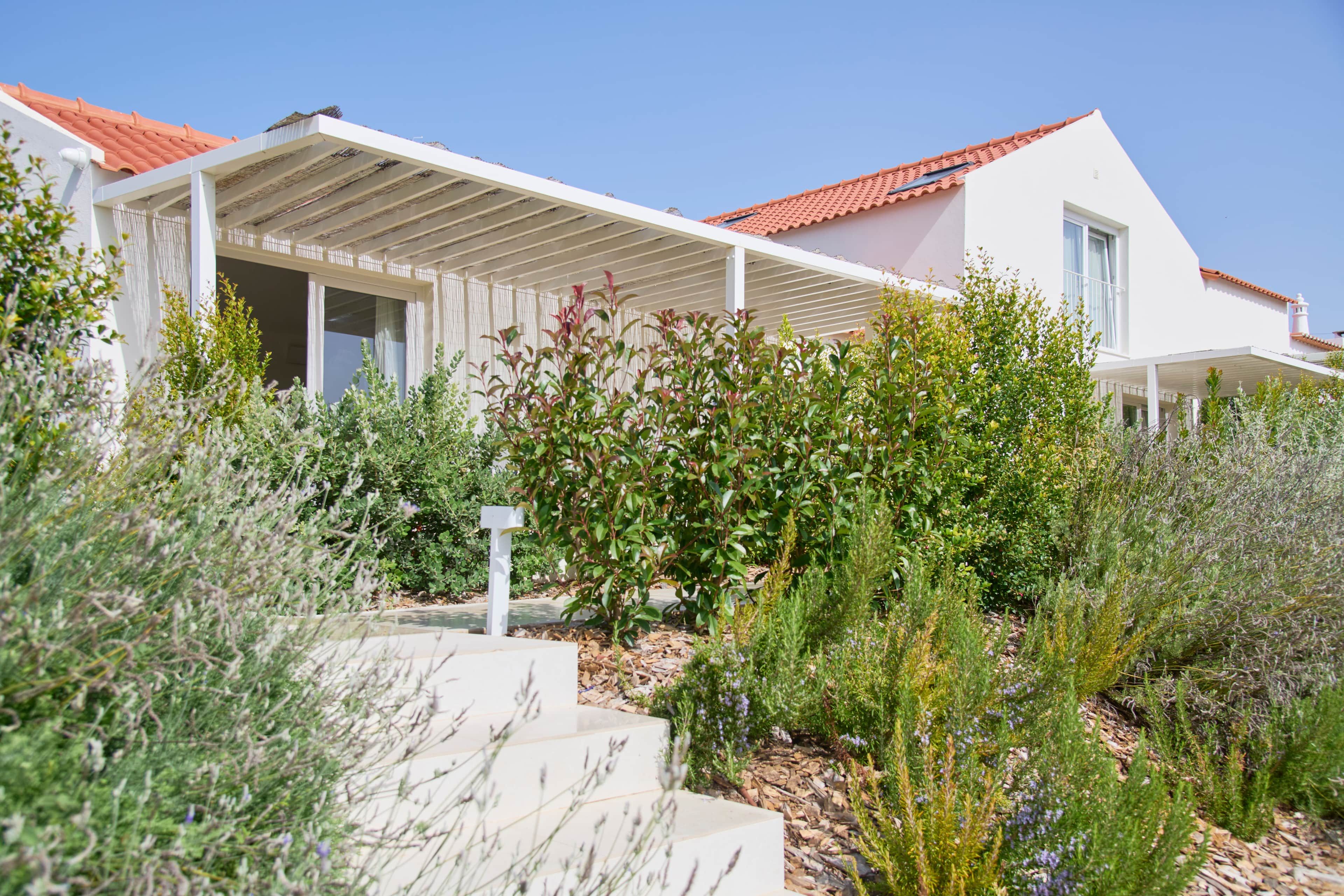 Una casa moderna amb teulada de rajola vermella, parets exteriors blanques i un porxo cobert.