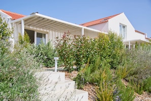 Une maison moderne avec un toit recouvert de tuiles rouges, des murs extérieurs blancs et un porche abrité.
