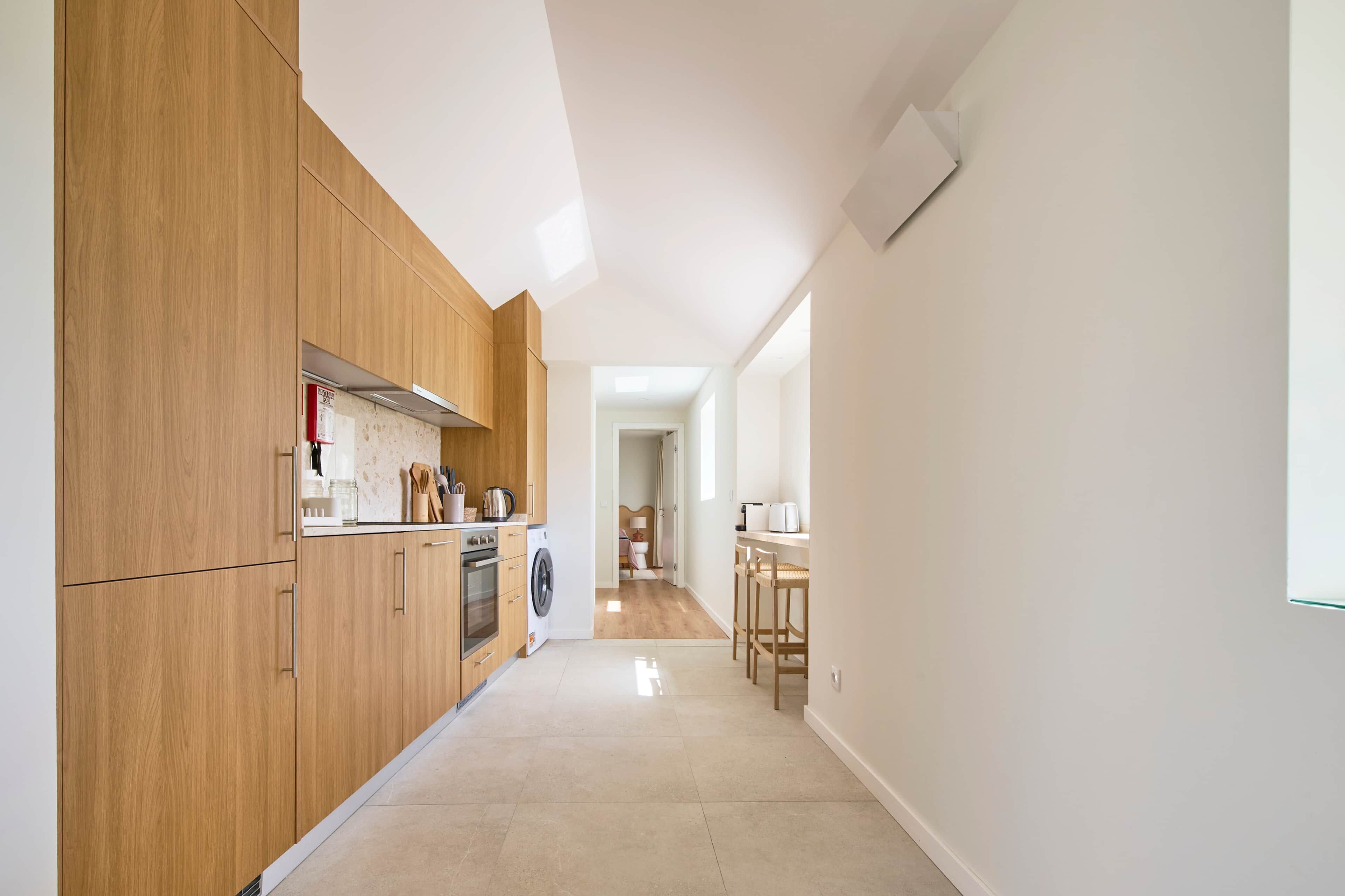 Una cocina moderna con armarios de madera, lavadora y zona de comedor con mesa y sillas.