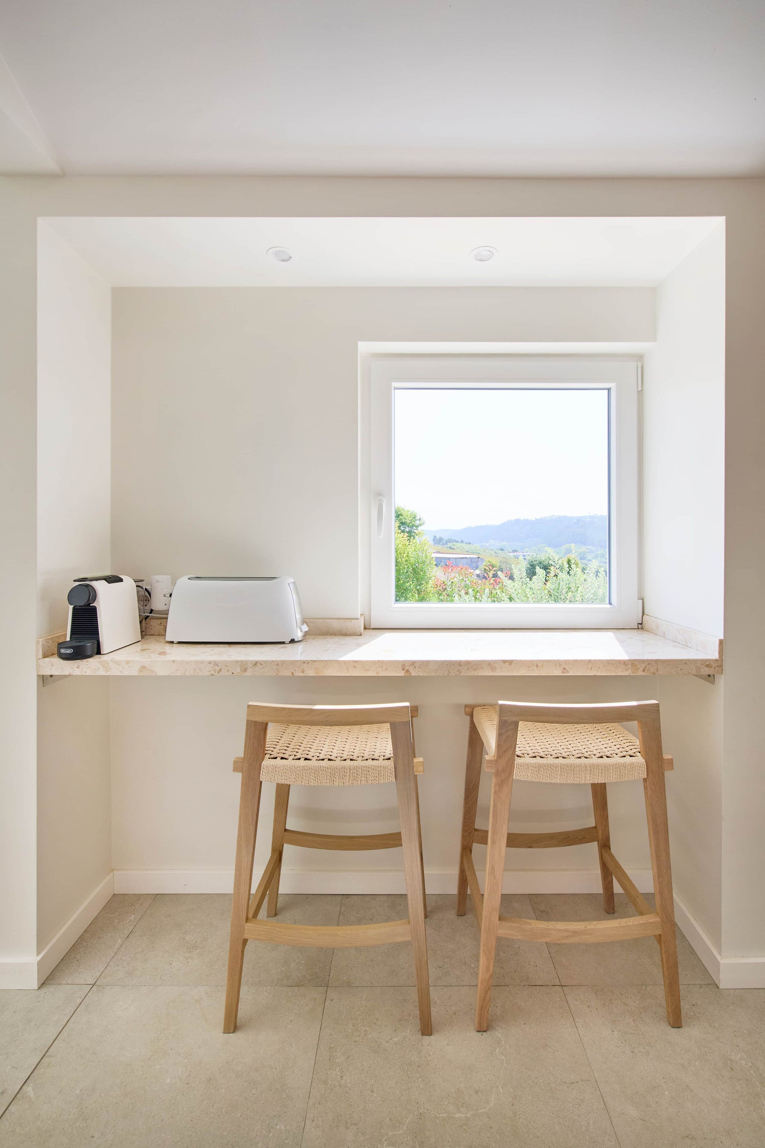 Una cocina con ventana, dos sillas de madera y un tostador sobre la encimera.