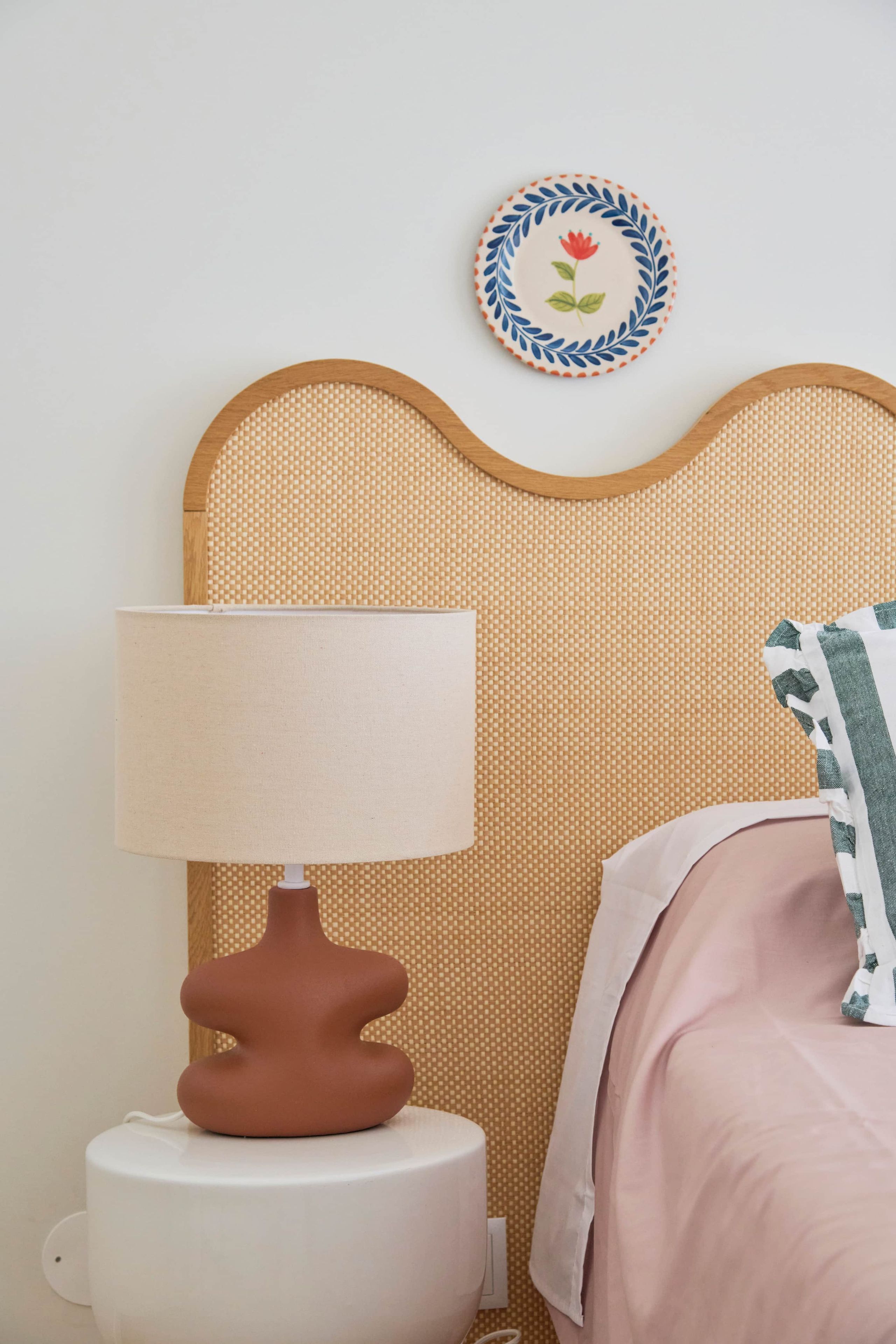 Una cama con cabecera, una lámpara de noche y un adorno floral en la pared.