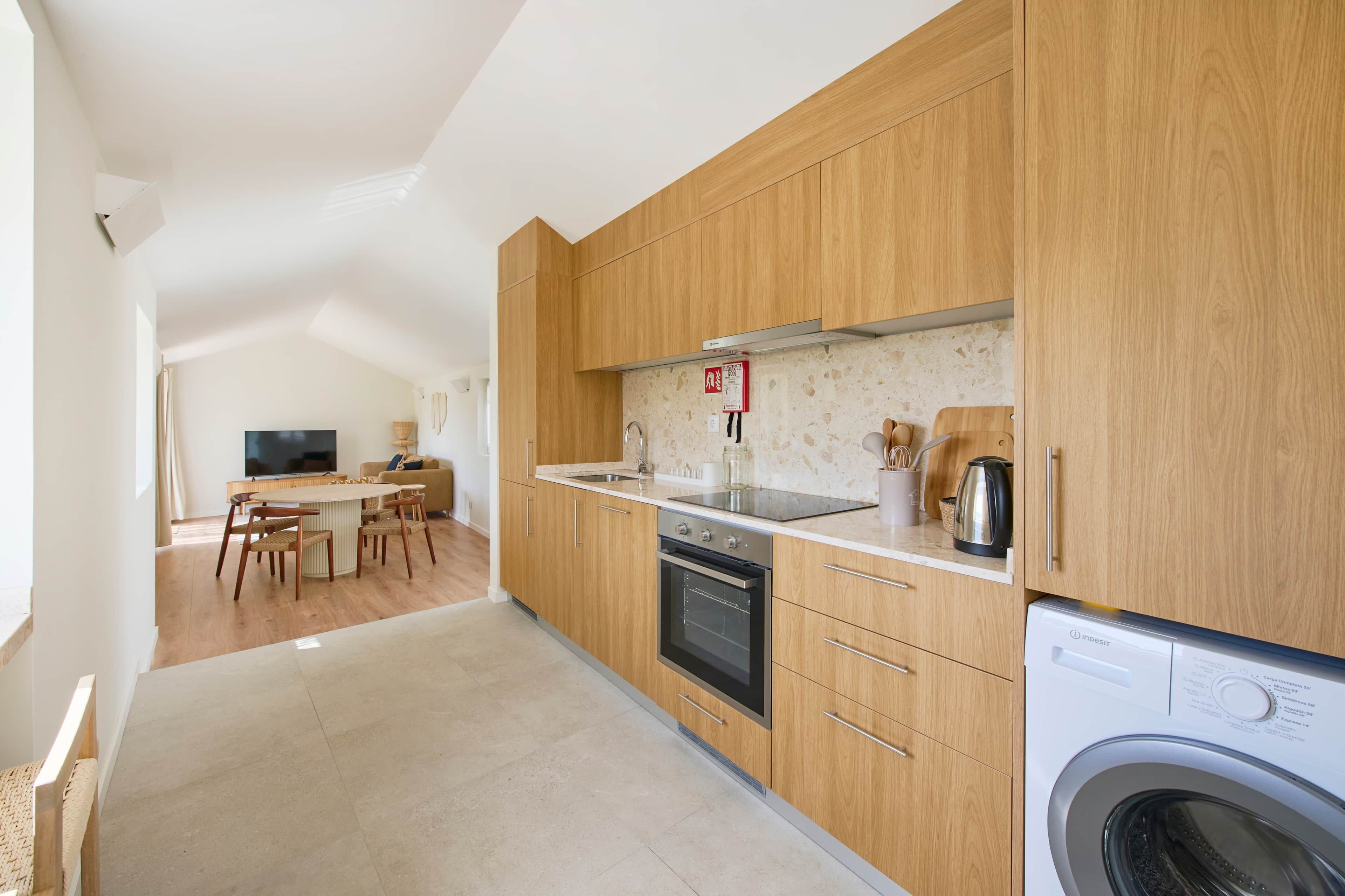 A modern kitchen with wooden cabinets, a built-in oven, and a washing machine.