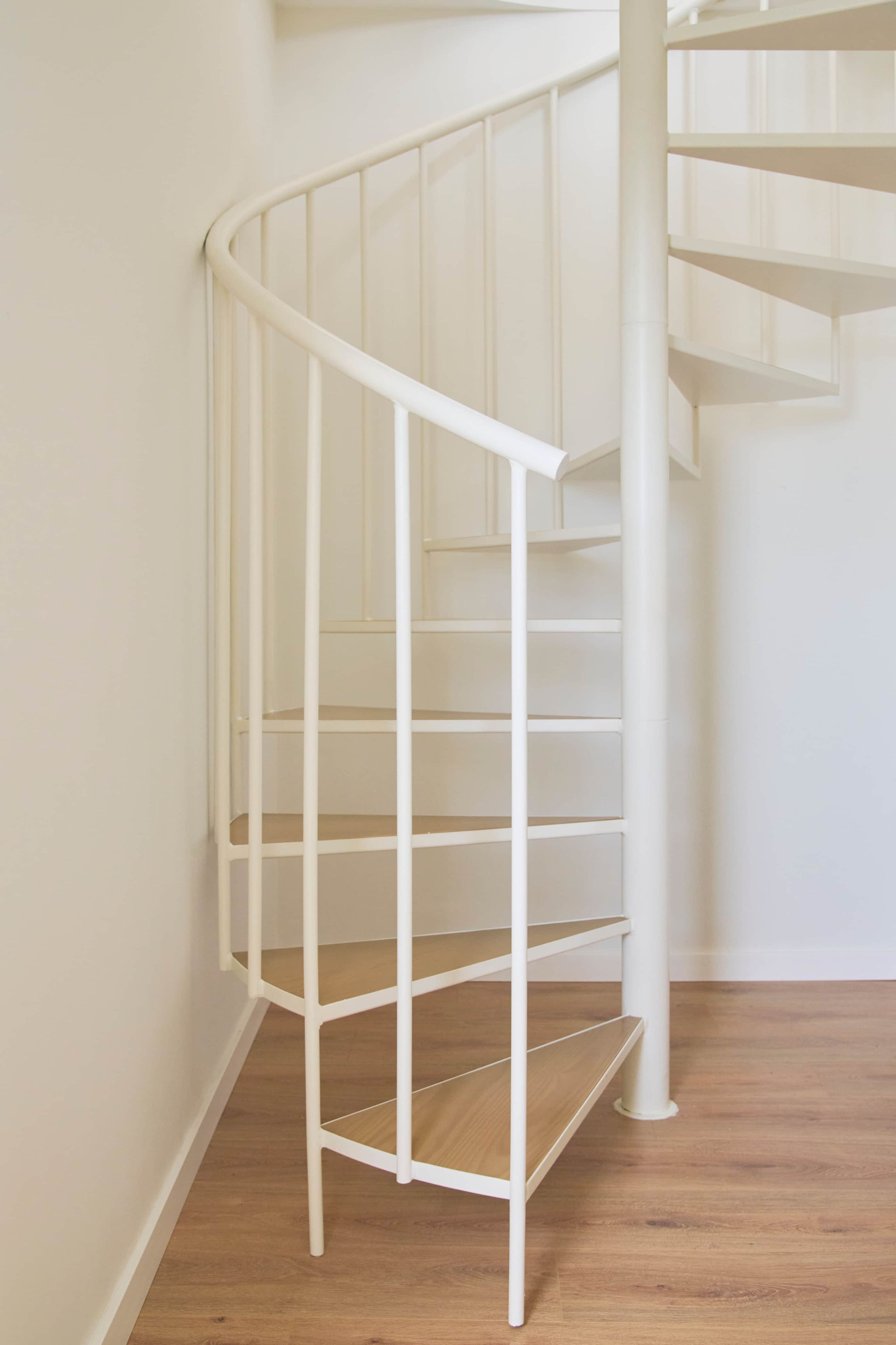 Een witte spiraaltrap met een houten vloer.