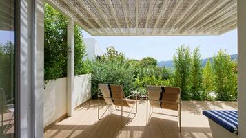 Un porxo cobert amb dues cadires i una taula, amb vistes a un jardí exuberant i a les colines llunyanes.