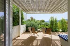 Une terrasse couverte avec deux chaises et une table, donnant sur un jardin luxuriant et sur des collines lointaines.