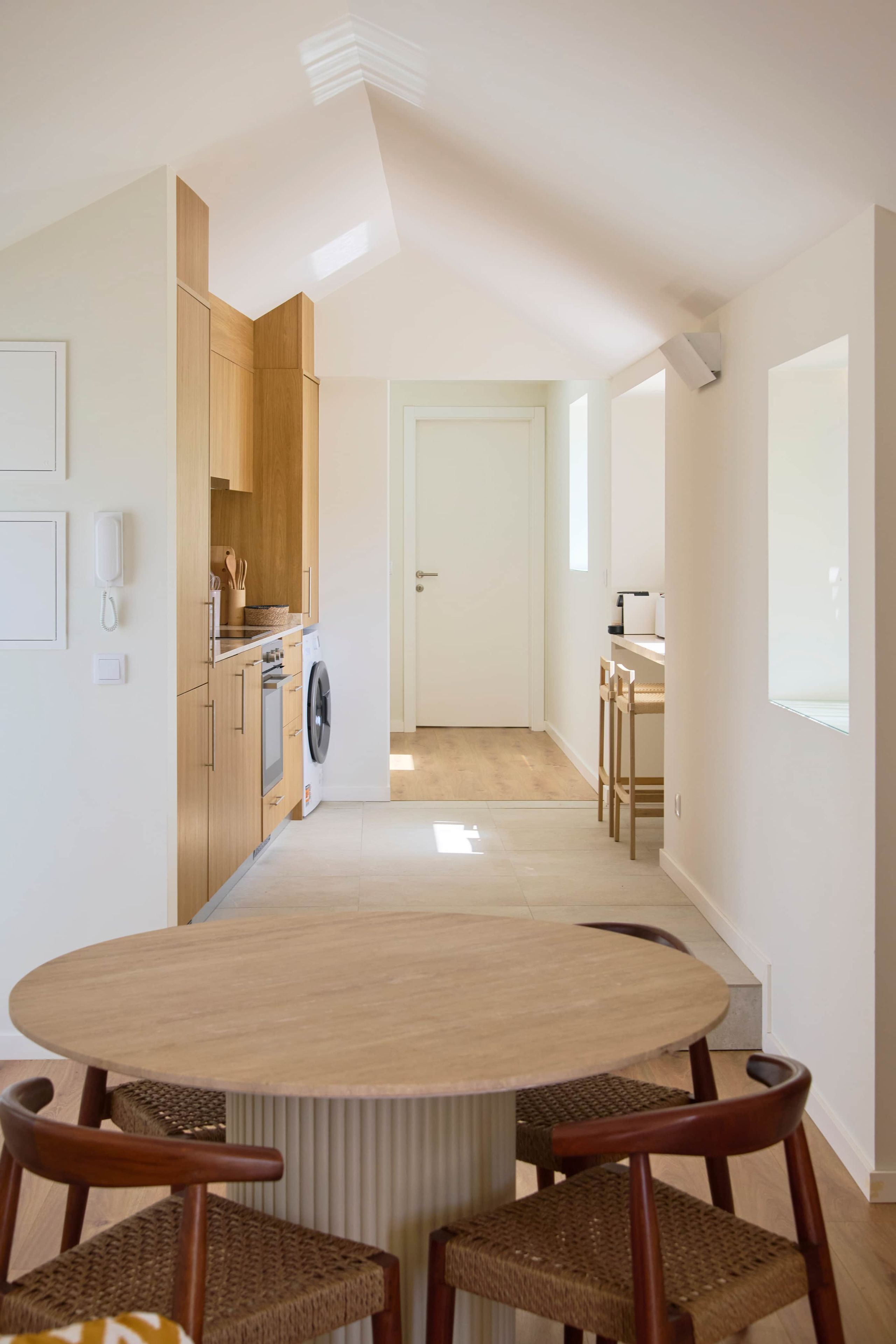 Una cocina moderna con armarios de madera, lavadora y un comedor con mesa redonda y sillas de mimbre.