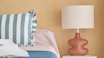Una cama bien tendida con un almohadón a rayas y una mesita de noche blanca con una lámpara.