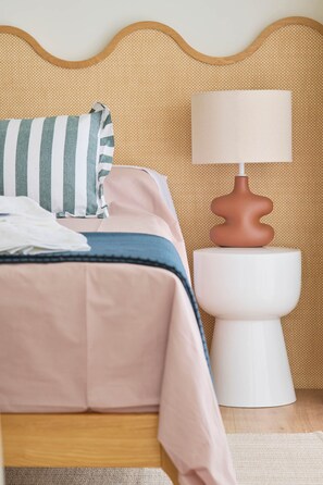 Een netjes opgemaakt bed met een gestreept kussen en een witte nachtkastje met een lamp.