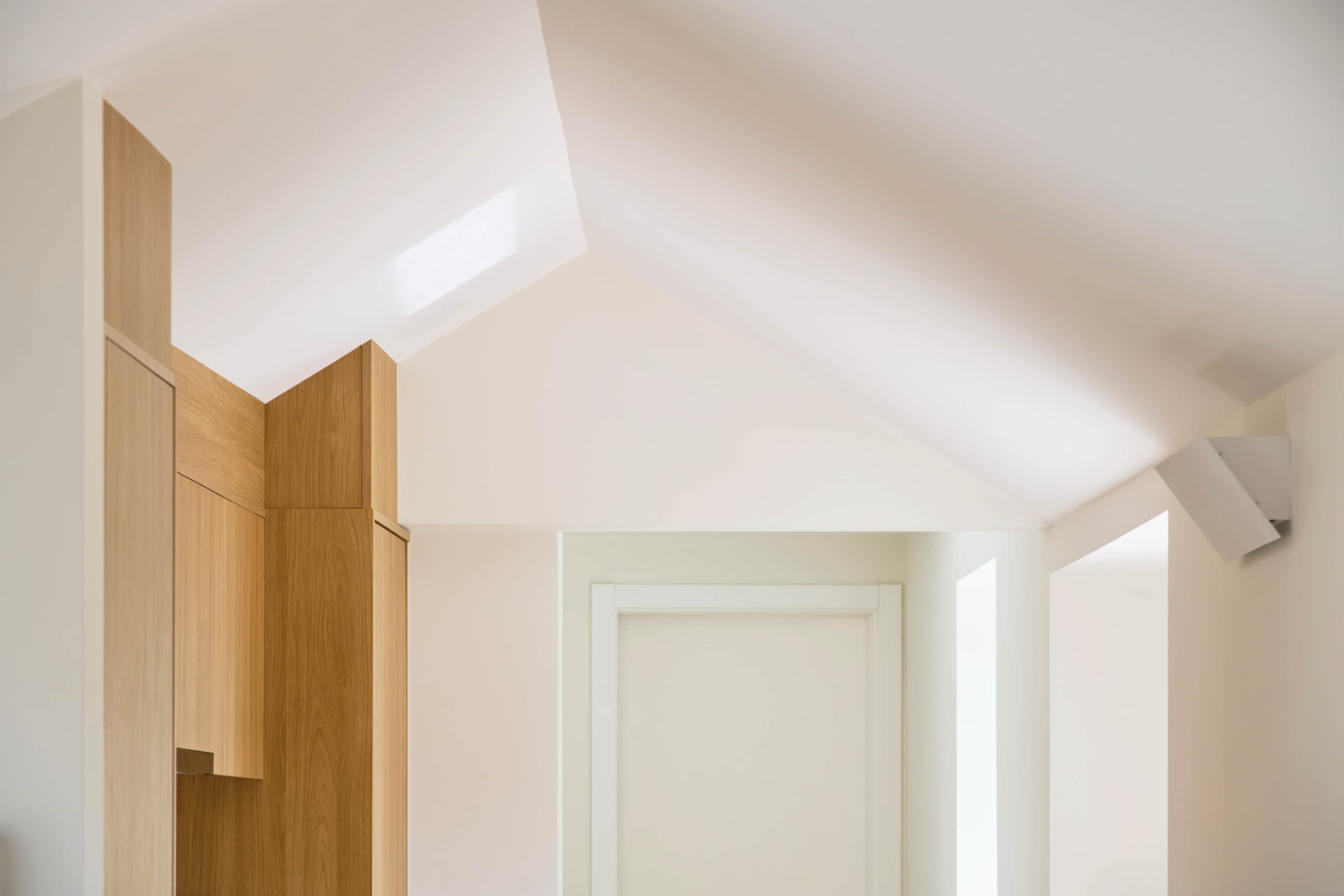 Una habitación con un armario de madera, una puerta blanca y un techo inclinado con tragaluces.