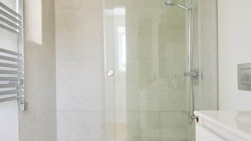 Un baño moderno con cabina de ducha de vidrio, inodoro blanco y alfombra color beige.