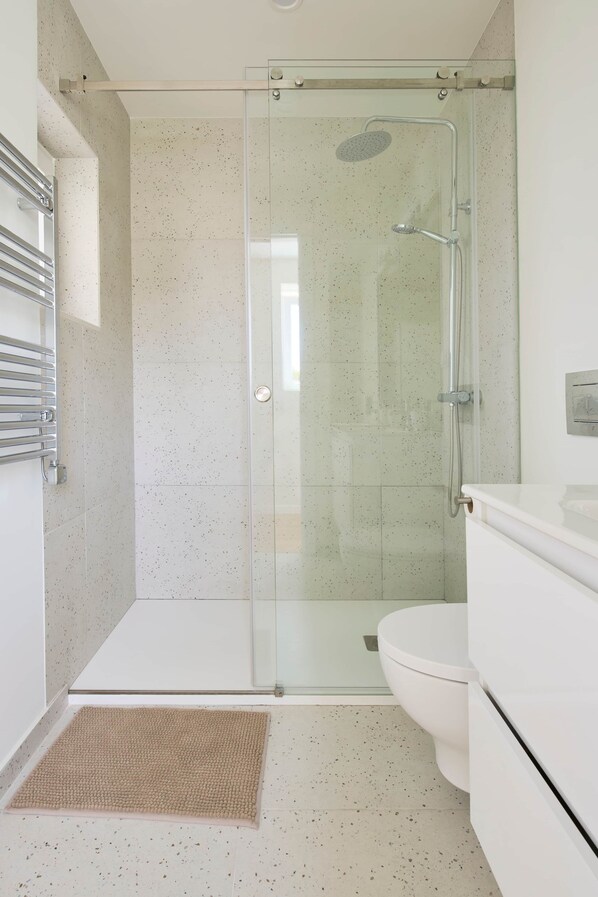 Een moderne badkamer met een douchecabine van glas, een wit toilet en een beige vloerkleed.