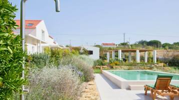 Zona de piscina amb vista clara a una casa, una estructura metàl·lica i una cadira de fusta.