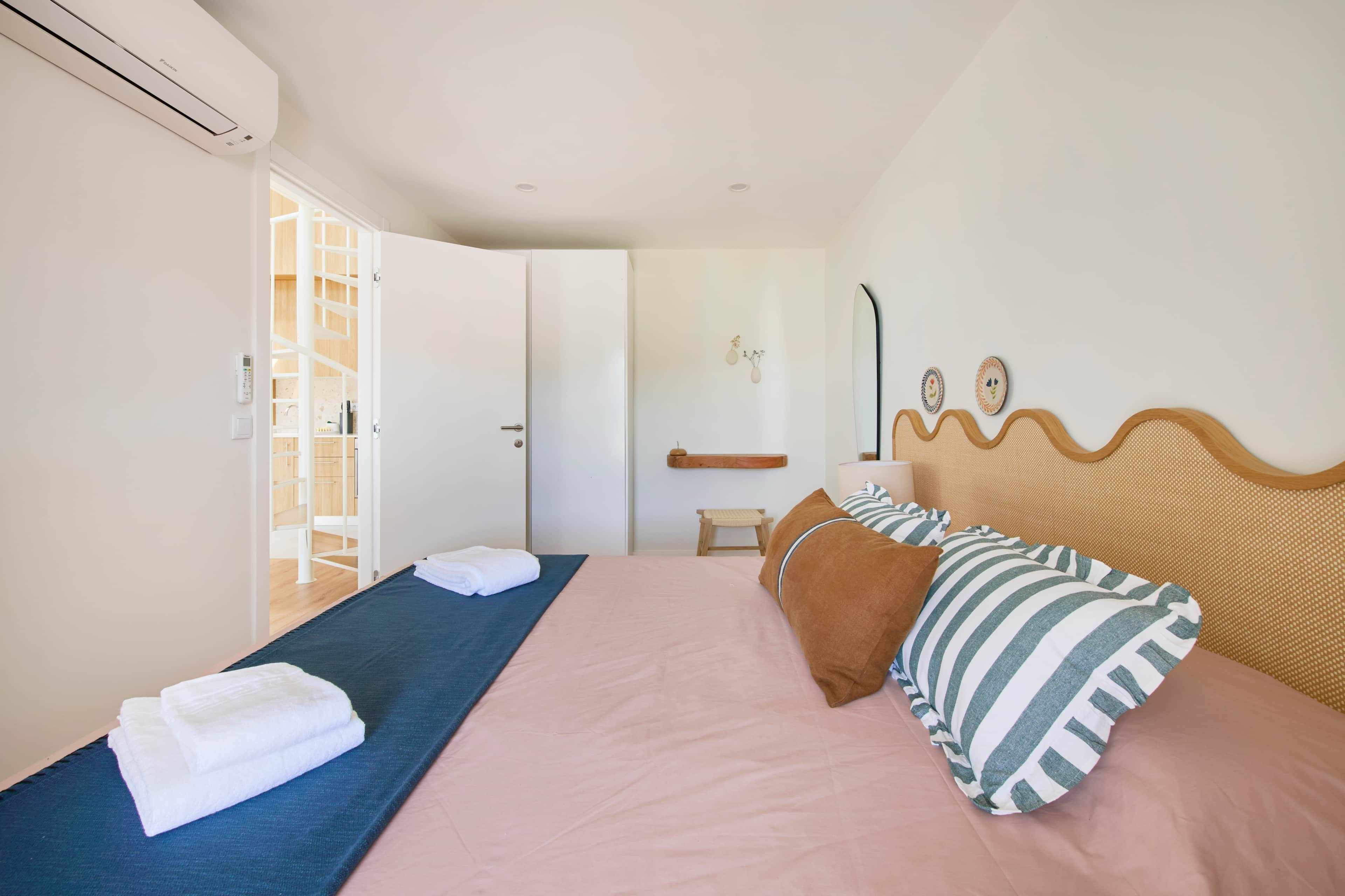 A bedroom with a bed, pillows, a bedside table, a mirror, and a wardrobe.