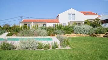 A two-story house with a red-tiled roof, a swimming pool, and a well-maintained garden.