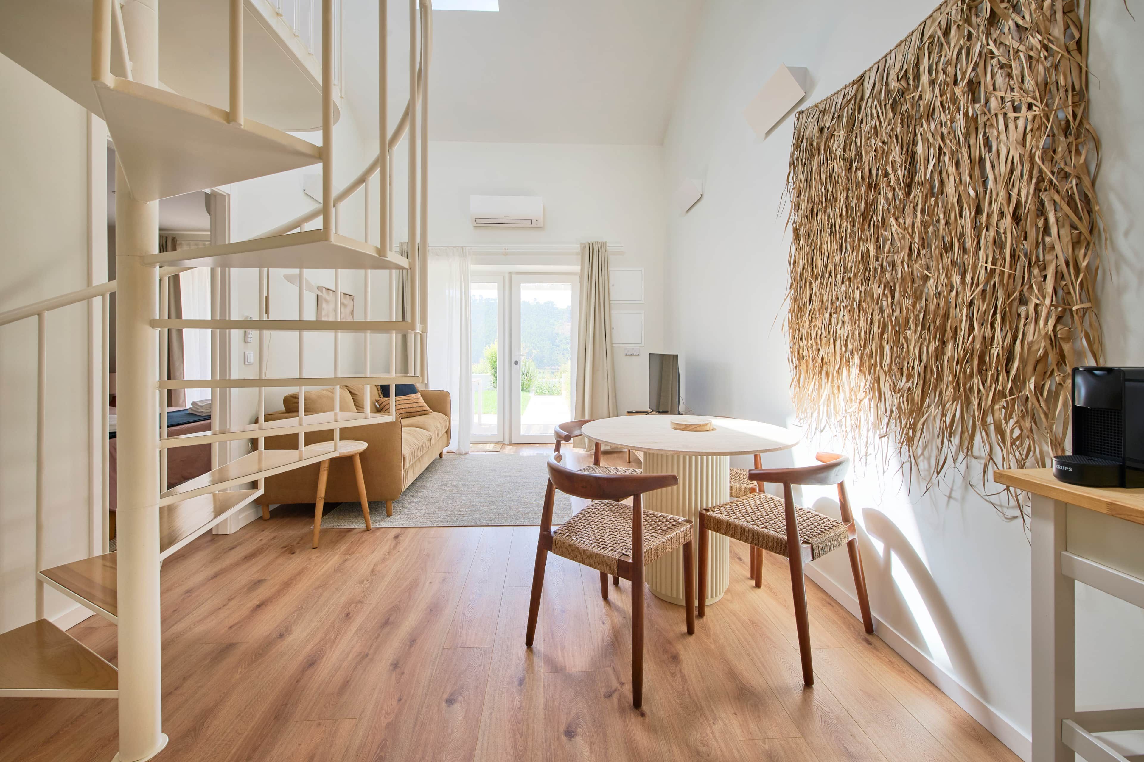 A modern interior with a wooden floor, a round table with chairs, a sofa, and a bookshelf.