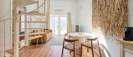 A modern interior with a wooden floor, a round table with chairs, a sofa, and a bookshelf.