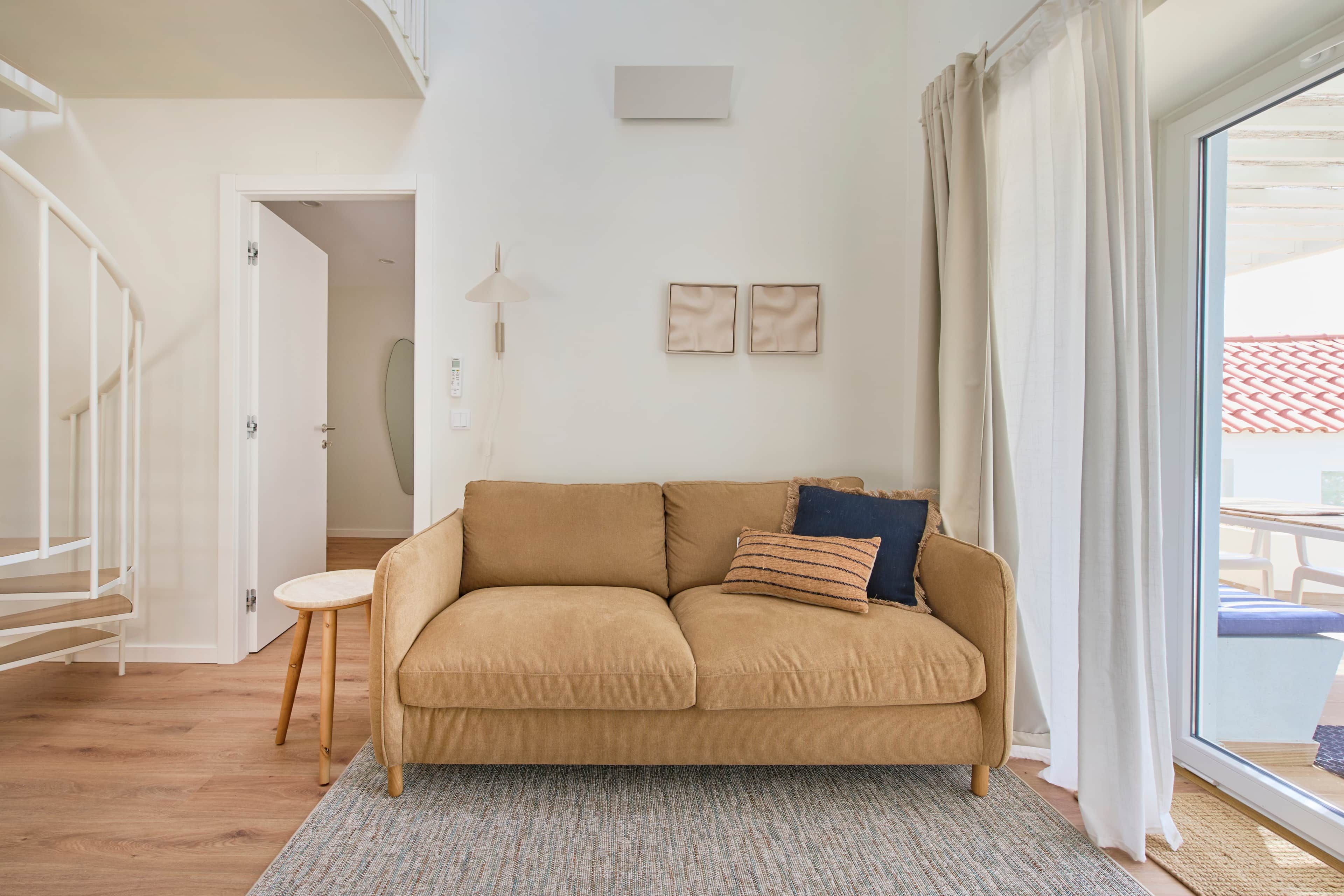 A living room with a beige sofa, a small round table, and a large window with curtains.