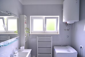 Een moderne badkamer met een wit wastafelmeubel, spiegel en handdoekrek. Boven het wastafelmeubel bevindt zich een raam en eronder een witte radiator.