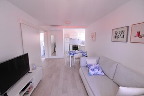 Een moderne woonkamer met een flatscreen televisie, een bank met een bloemenkussen en een eethoek met een tafel en stoelen.