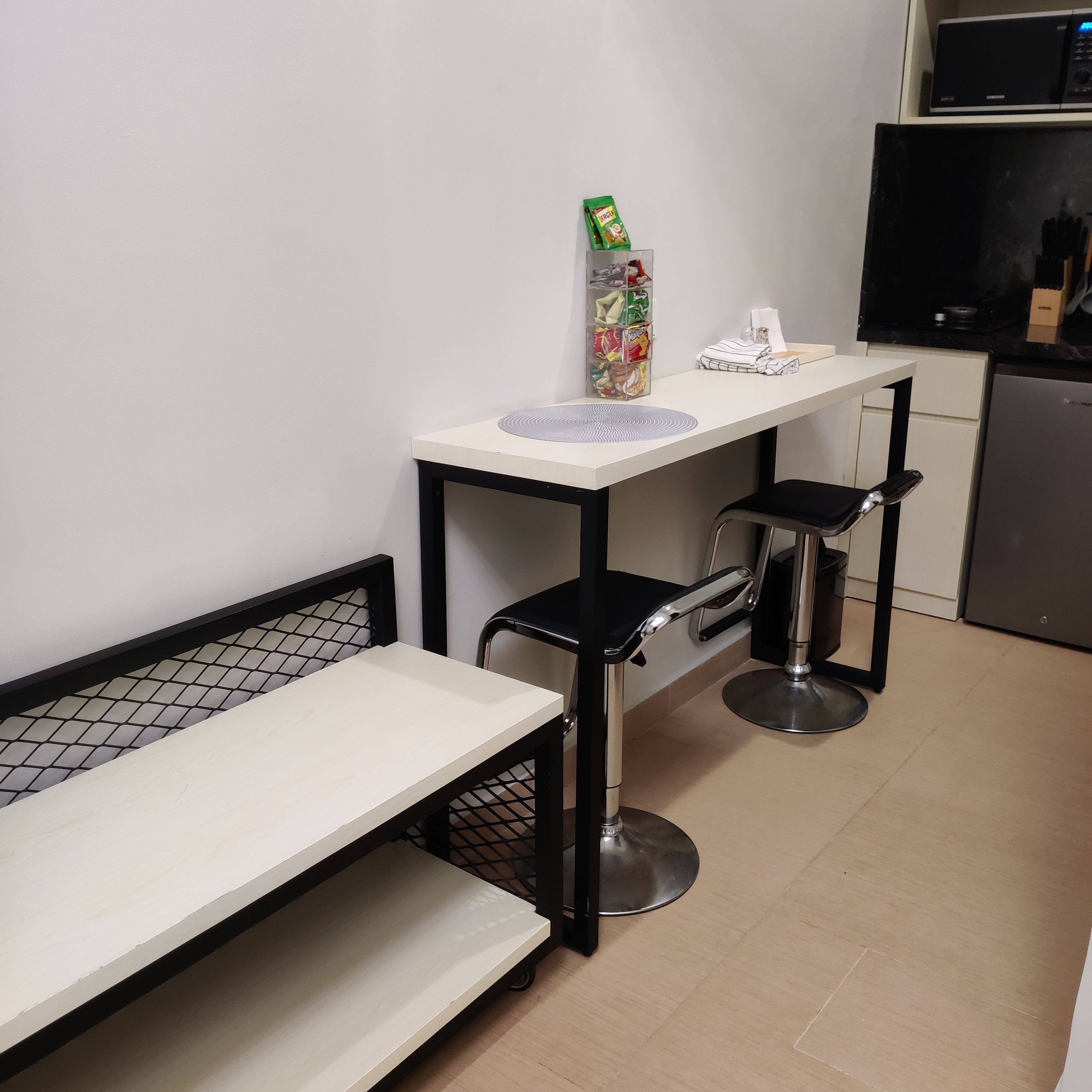 Una kitchenette con microondas, un refrigerador pequeño, una encimera blanca y una banca.