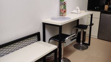 Una kitchenette con microondas, un refrigerador pequeño, una encimera blanca y una banca.