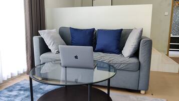 Ein modernes Wohnzimmer mit einem grauen Sofa, einem Glastisch und einem Apple Laptop.