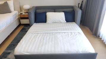 Una habitación de hotel moderna con una cama grande, una mesita de noche con lámpara y vistas al exterior.