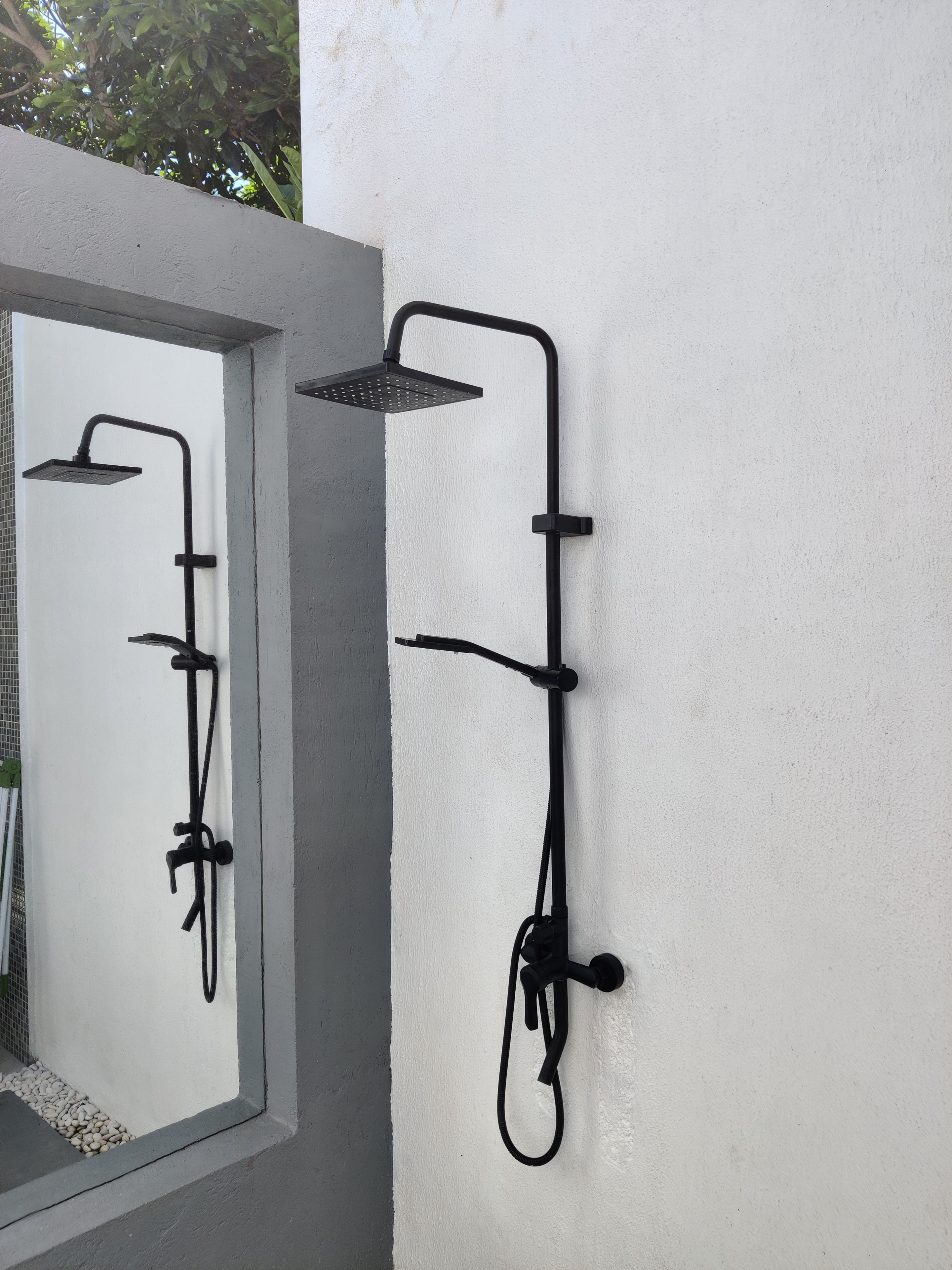 A modern outdoor shower setup with a rain shower head and a handheld shower attachment mounted on a white wall.