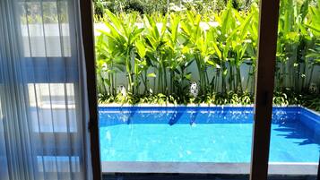 Vista despejada de una piscina con borde de azulejos, rodeada de exuberante vegetación y una pared blanca.