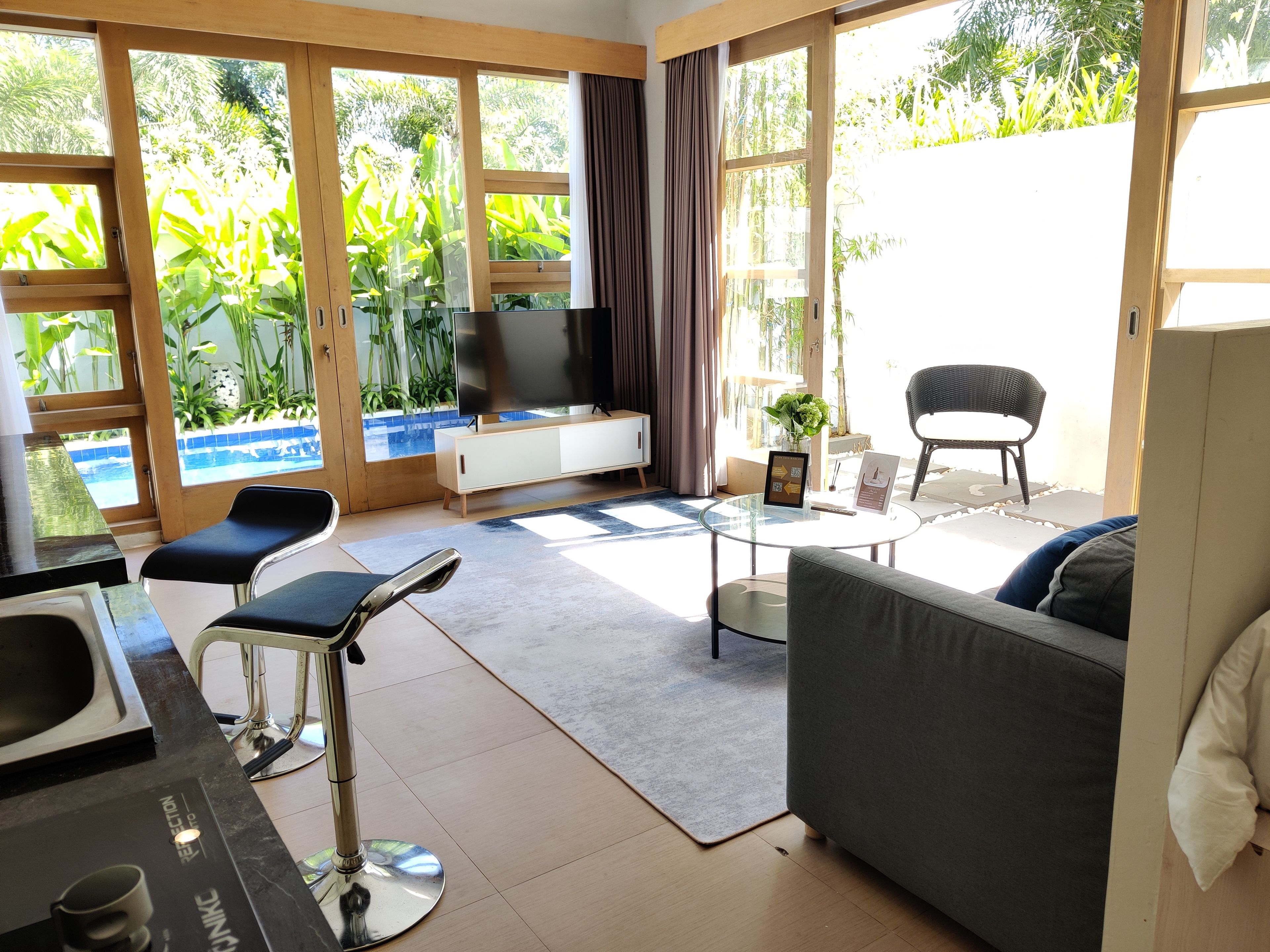 Ein modernes Wohnzimmer mit Fernseher, Sitzgelegenheiten und Blick auf einen Pool.