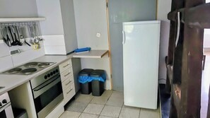 Cocina compacta con estufa, horno y refrigerador. Hay dos botes de basura con tapas azules.