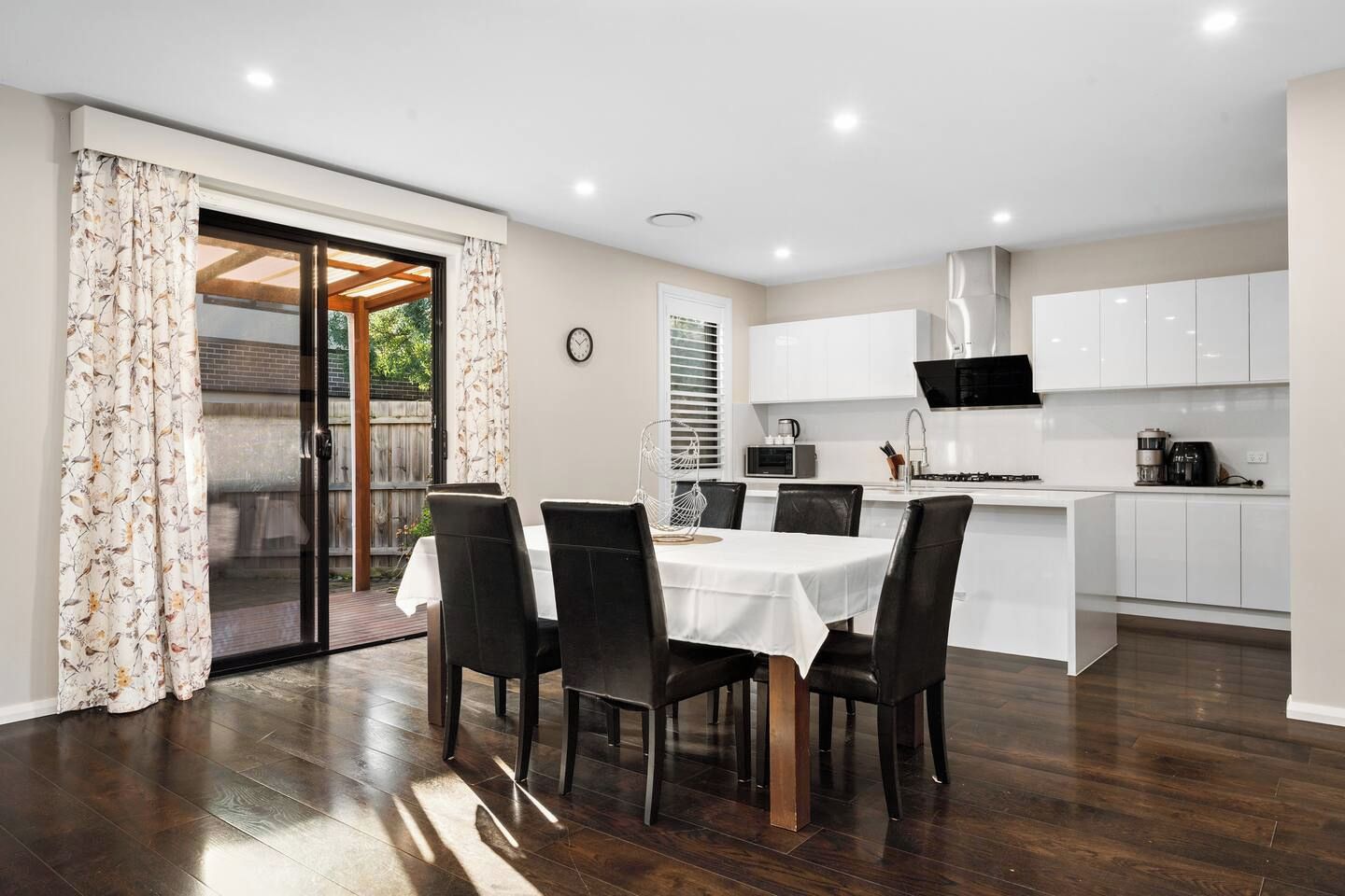 A modern kitchen with white cabinets, a dining area with a round table and chairs, and a sliding glass door leading to an outdoor space.