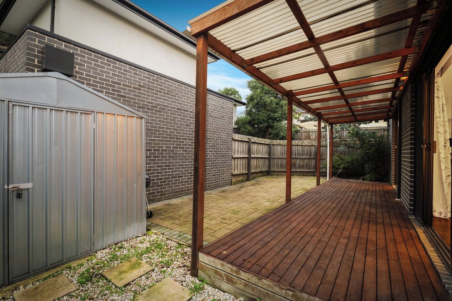 A covered patio area with a wooden deck and a metal fence.